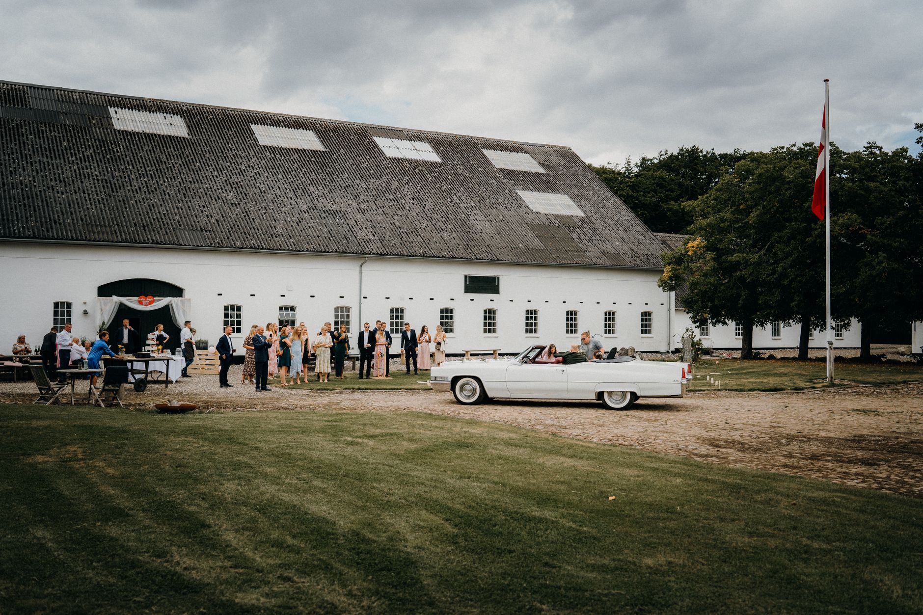 Guests in fall country wedding attire with tweed vests, boots and warm-toned dresses outside a barn