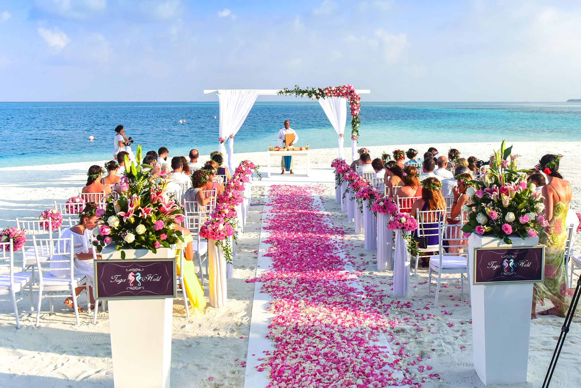 Wedding guests in light linen suits and flowing dresses at a beach ceremony