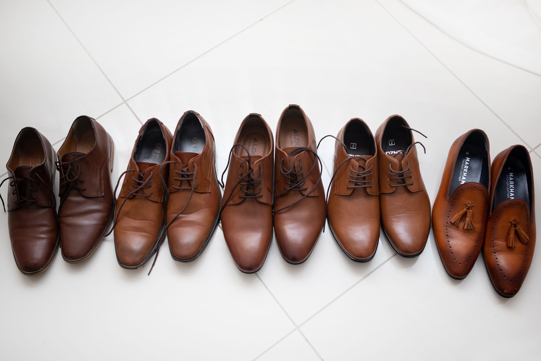 Brown loafers, black derby shoes and suede chukka boots lined up on a wood floor